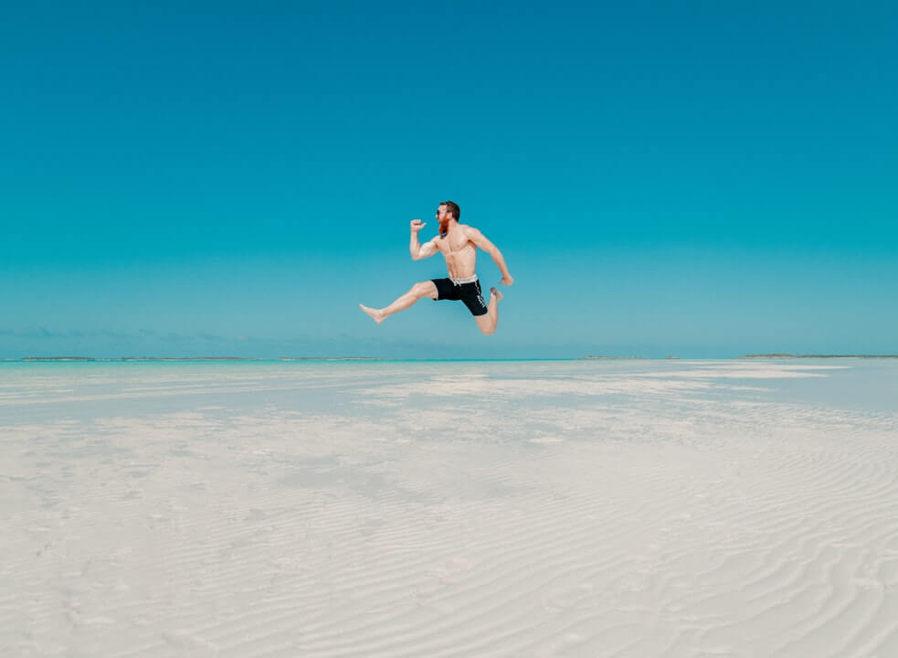 A man in black shorts jumping over a sandbar.