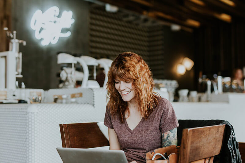 A woman in a coffee shop smiling at her laptop.