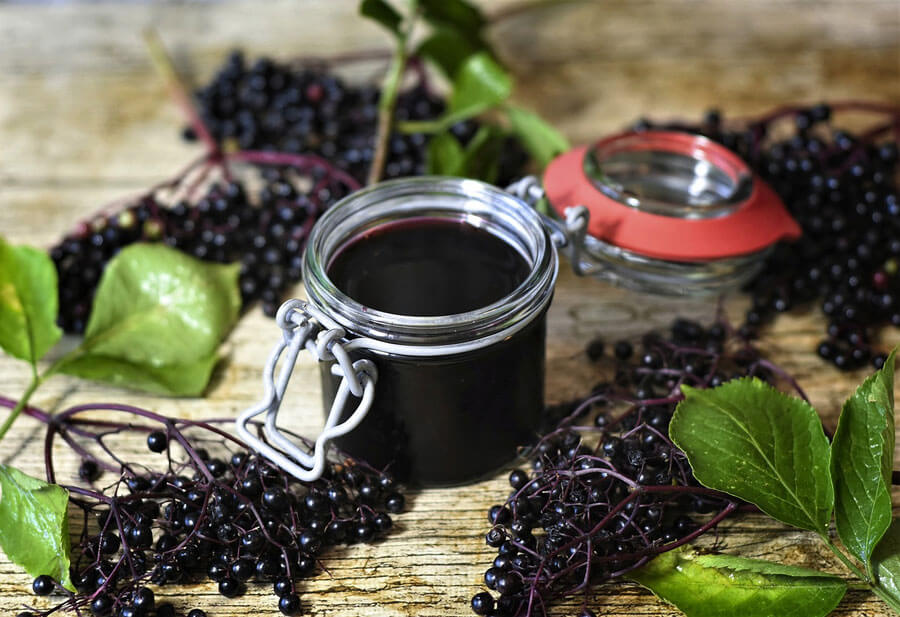 A mason jar of elderberry syrup surrounded by bunches of elderberries